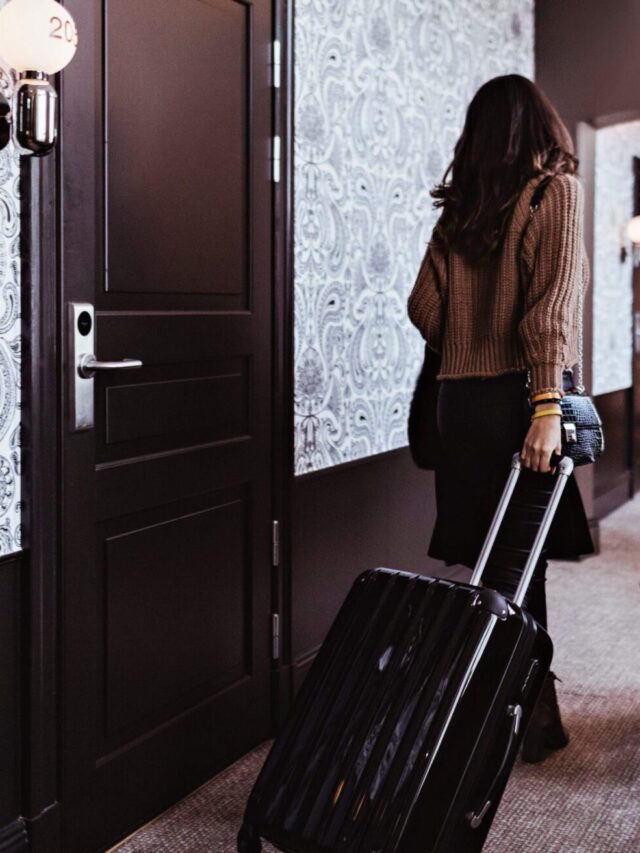 THEME_TRAVEL_HOTEL_CORRIDOR_ROOMS_PEOPLE_COUPLE_WALKING_LUGGAGE_GettyImages-1241453705-scaled